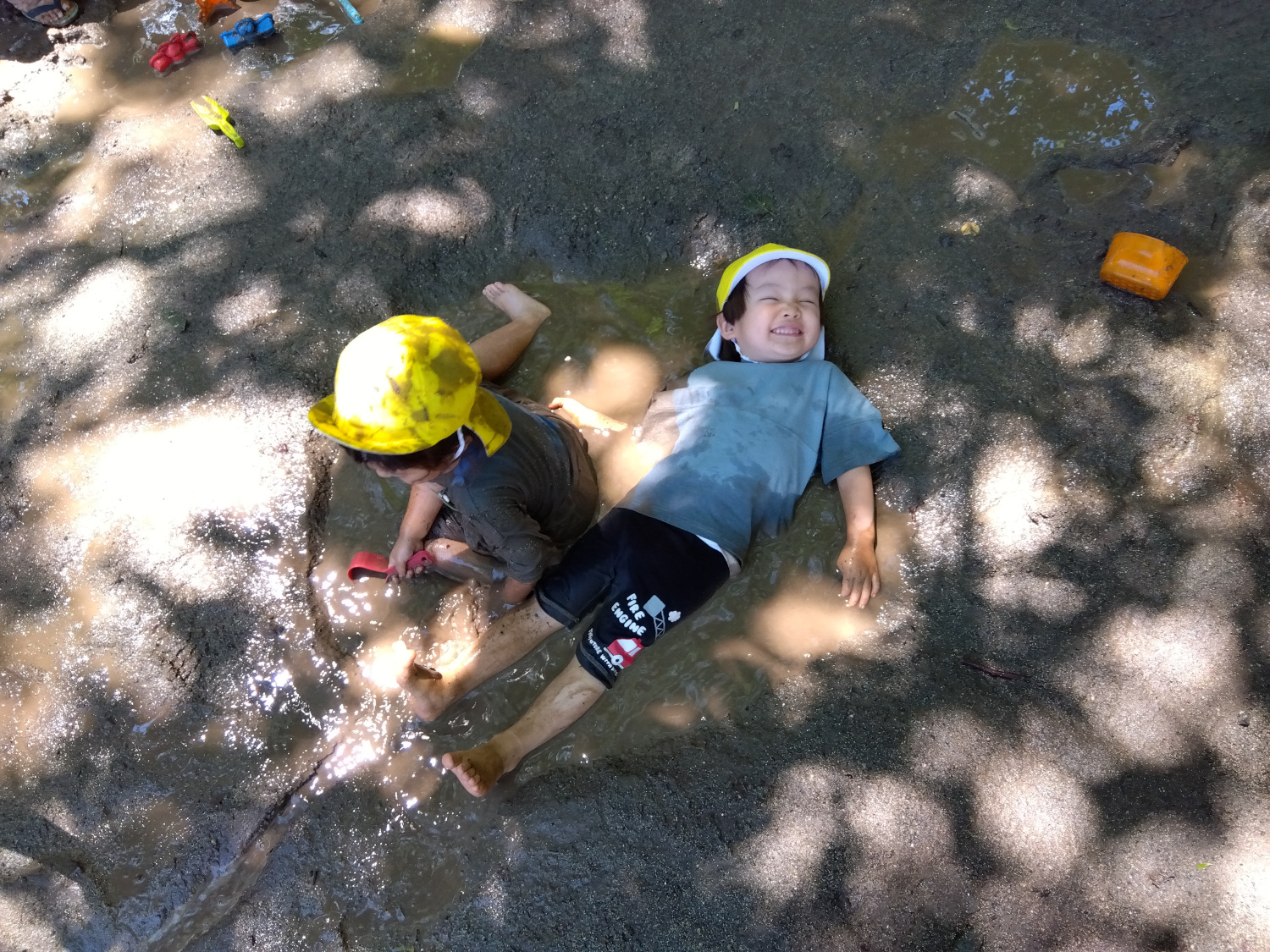 砂場の水たまりで泥だらけになる子どもたち