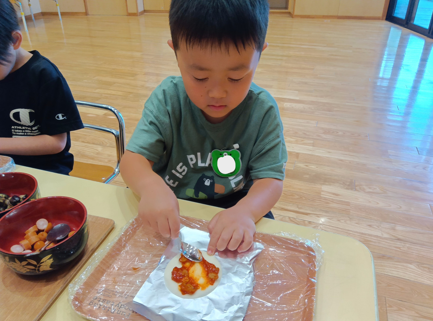 餃子の皮にピザソースをのせる子ども