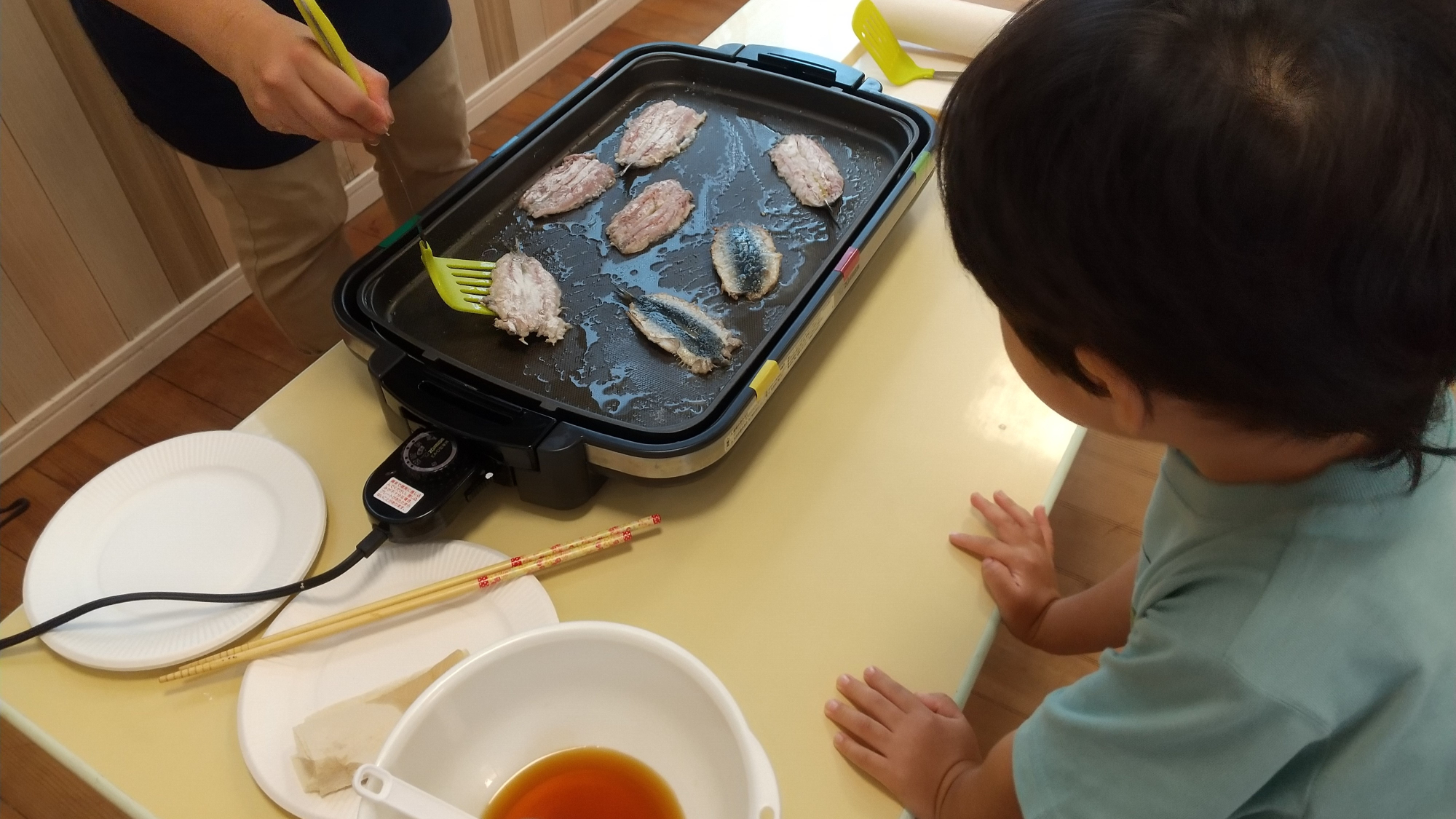 焼かれるイワシに興味津々の子ども