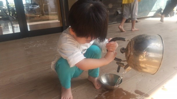 やかんから器に水を移し替えようとする子ども