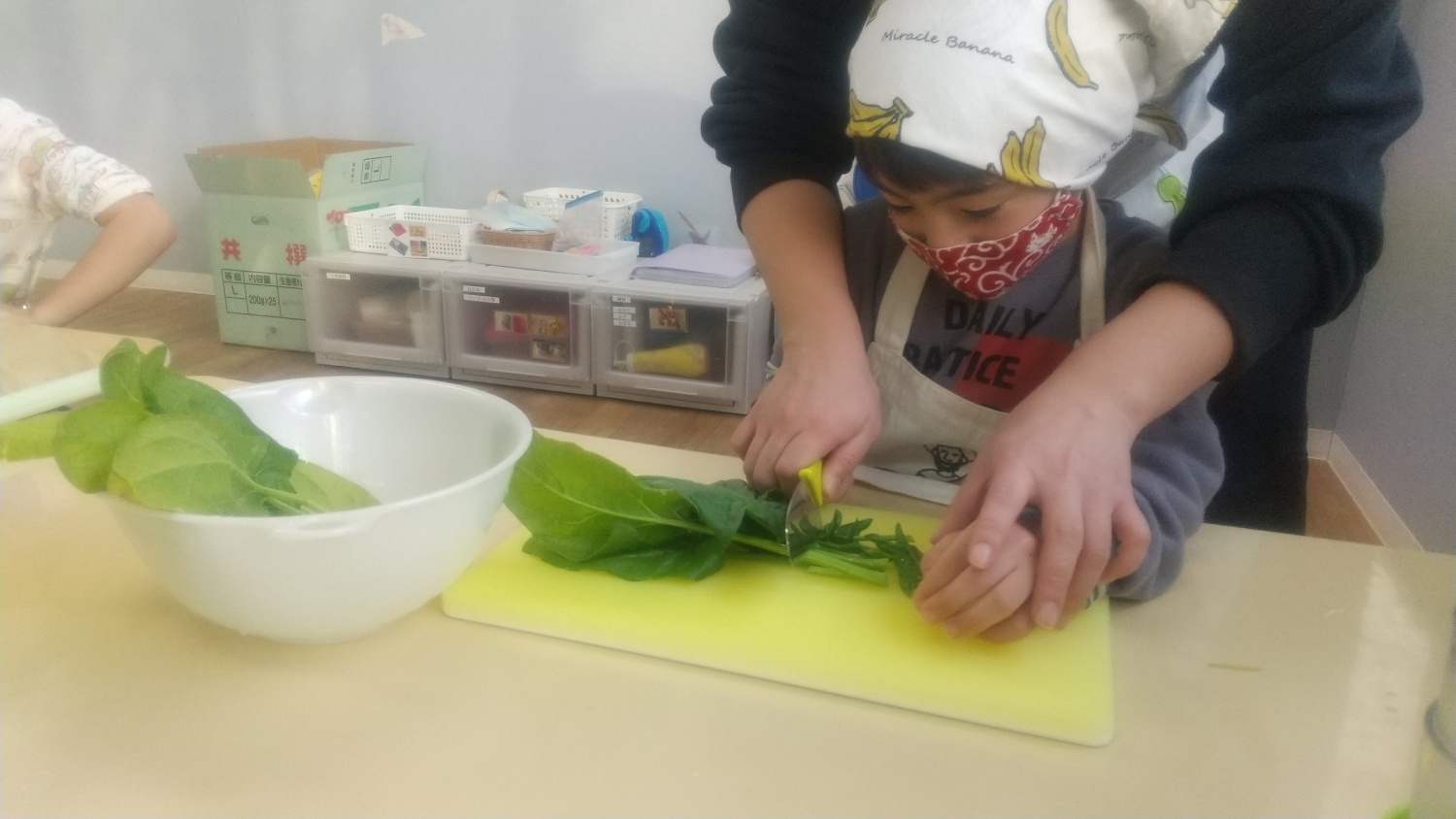 包丁を使ってほうれん草を切る子ども